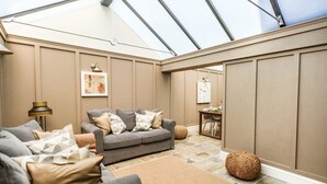 A modern living room with a grey sofa, a dining table, and a large window. - The Apple Loft at Jordan House (Weymouth)