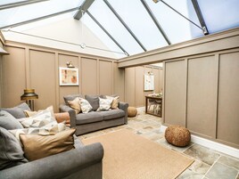 A modern living room with a grey sofa, a dining table, and a large window.