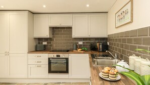 A modern kitchen with white cabinets, a built-in oven, a microwave, and a sink. There are decorative items on the counter and a framed picture on the wall. - The Apple Loft at Jordan House (Weymouth)
