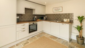A modern kitchen with white cabinets, a built-in oven, a microwave, and a sink. There's a decorative tile backsplash and a framed picture on the wall. - The Apple Loft at Jordan House (Weymouth)