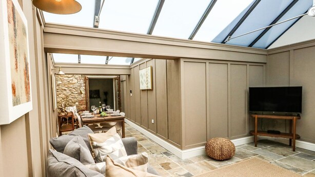 A spacious living room with a high ceiling, a dining area, and a television on a wooden stand. - The Apple Loft at Jordan House (Weymouth)
