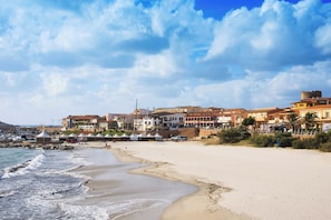 Un pueblo costero con una playa arenosa, edificios con balcones y una estructura tipo torre.
