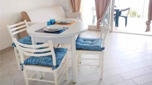 Ein Essbereich mit einem runden Tisch, weißen Stühlen mit blauen Kissen und einer Couch.