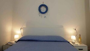 A bedroom with a bed, two bedside tables, a wall-mounted air conditioner, and a coiled cable on the wall. - Holiday apartment close to the beach (Santa Teresa di Gallura)
