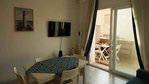 A dining area with a table and chairs, a flat-screen TV mounted on the wall, and a view of an outdoor balcony with a table and chairs. - Holiday apartment close to the beach (Santa Teresa di Gallura)