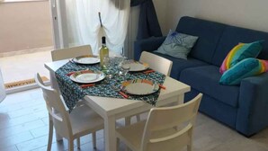 A dining area with a table set for four, a blue sofa with colorful cushions, and a door leading outside. - Holiday apartment close to the beach (Santa Teresa di Gallura)