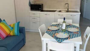 A modern kitchen with white cabinets, a black microwave, and a sink. A dining table with a colorful tablecloth is set with plates and cutlery. - Holiday apartment close to the beach (Santa Teresa di Gallura)