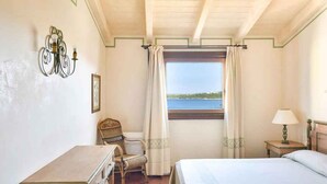 Ett sovrum med en säng, ett skrivbord, en stol, ett fönster med utsikt över havet och en vägglampa.
