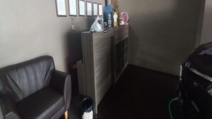 A room with a black leather sofa, a wooden cabinet with framed certificates, and a motorcycle charging. - OYO 93668 Buah Batu Guest House (Bandung)