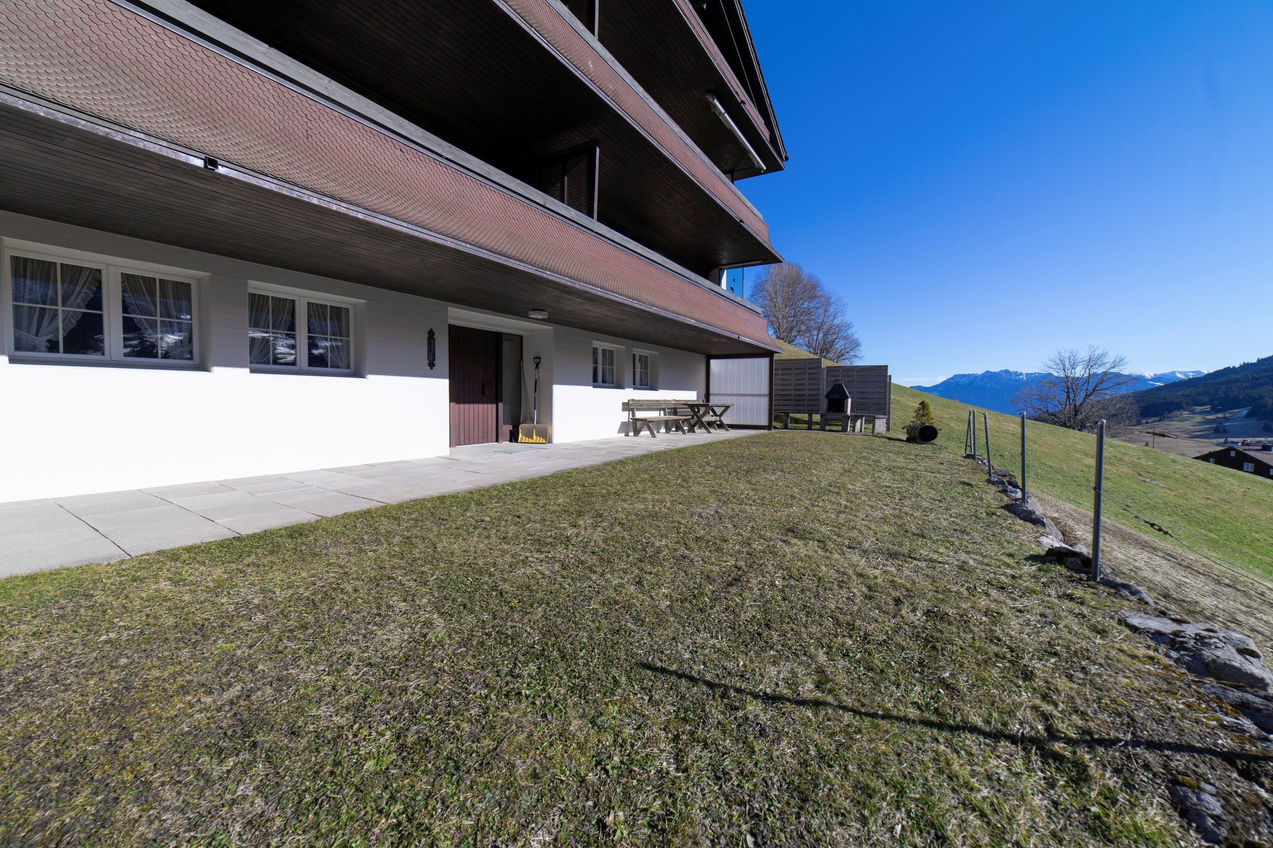 Un edificio de dos pisos con techo plano, un porche cubierto y un patio con césped.