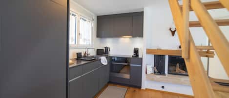 A compact kitchen with modern appliances, a wooden staircase, and a view of the outdoors.