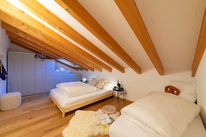A bedroom with a loft-style ceiling, wooden beams, a bed, a desk, and a wardrobe.