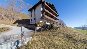 Un edificio de varios pisos con techo inclinado, una escalera que lleva a la entrada y un cielo despejado.