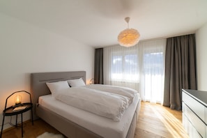 Et soveværelse med en seng, et natbord med lampe, en kommode og et vindue med gardiner.