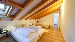 Un dormitorio con techo inclinado, vigas de madera, una cama, mesitas de noche y un escritorio con una lámpara.