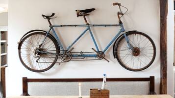 Una mesa de madera rústica con una vela y una caja de madera con la etiqueta 'BERNARD PEGLAR WHOLESALE FISH MERCHANTS' en una habitación con vigas de madera a la vista y una bicicleta colgada en la pared.