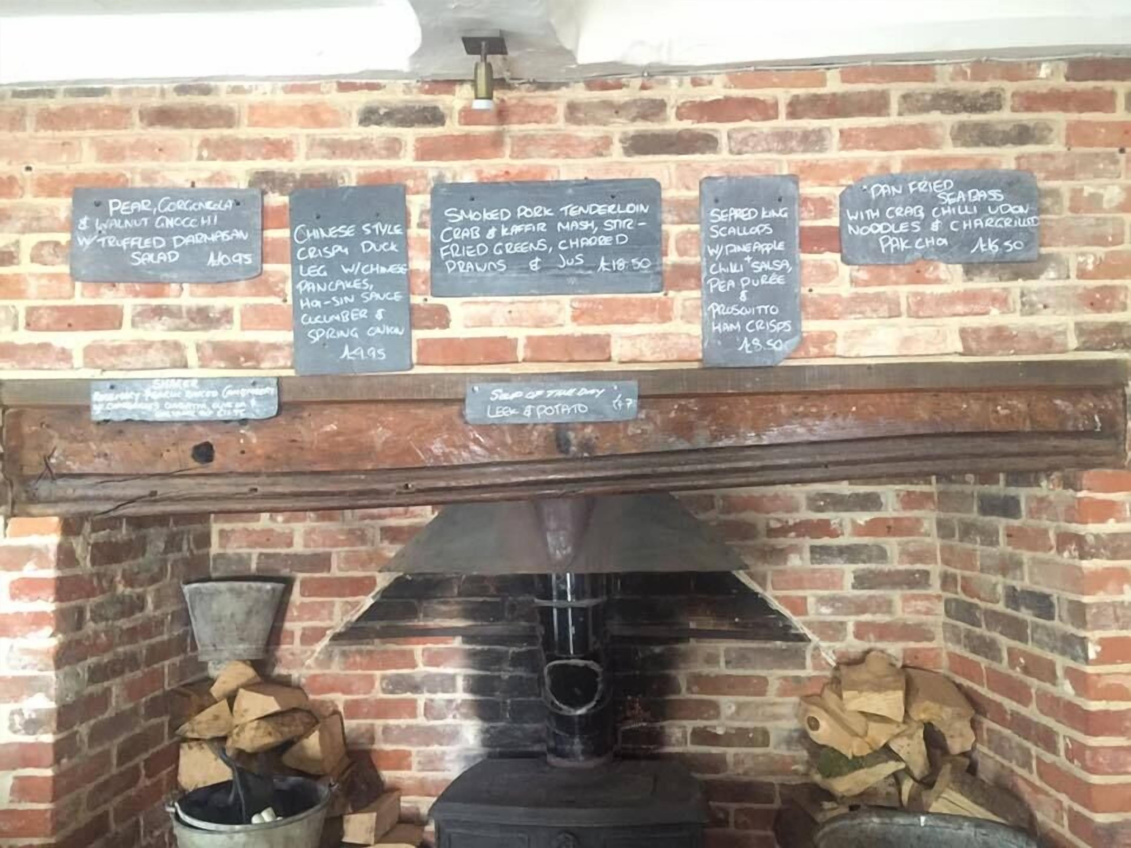 A brick wall with menu boards listing various dishes and prices.
