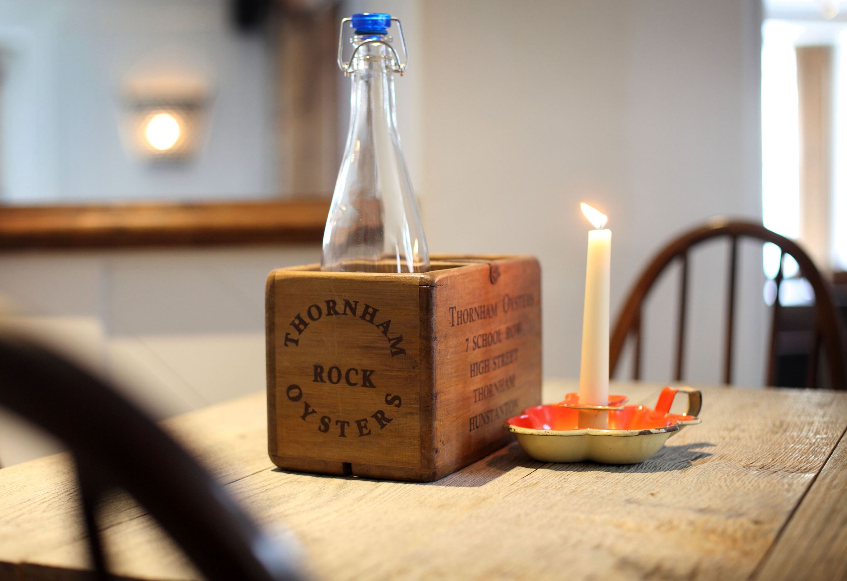 A wooden box labeled "Thornham Rock Oyster" with a candle and a bowl of fruit on a table.