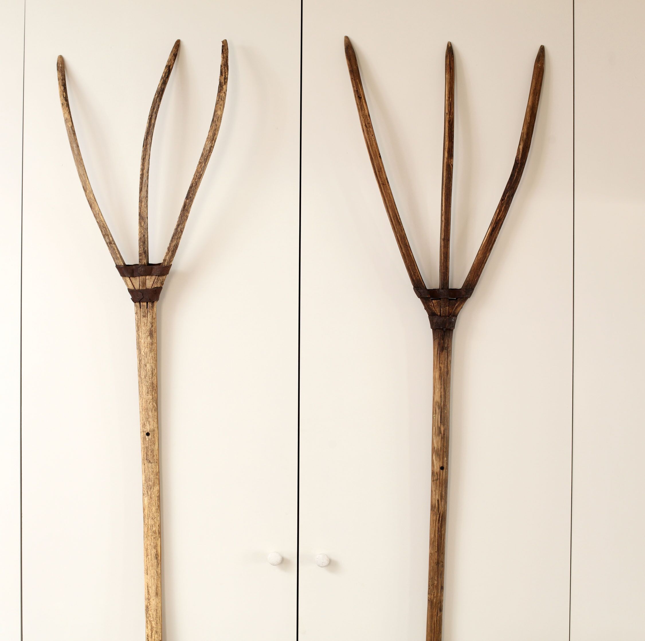 Two identical wooden pitchforks against a plain background.