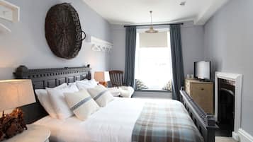 A neatly arranged bedroom with a large bed, a television, a fireplace, and a window with curtains.