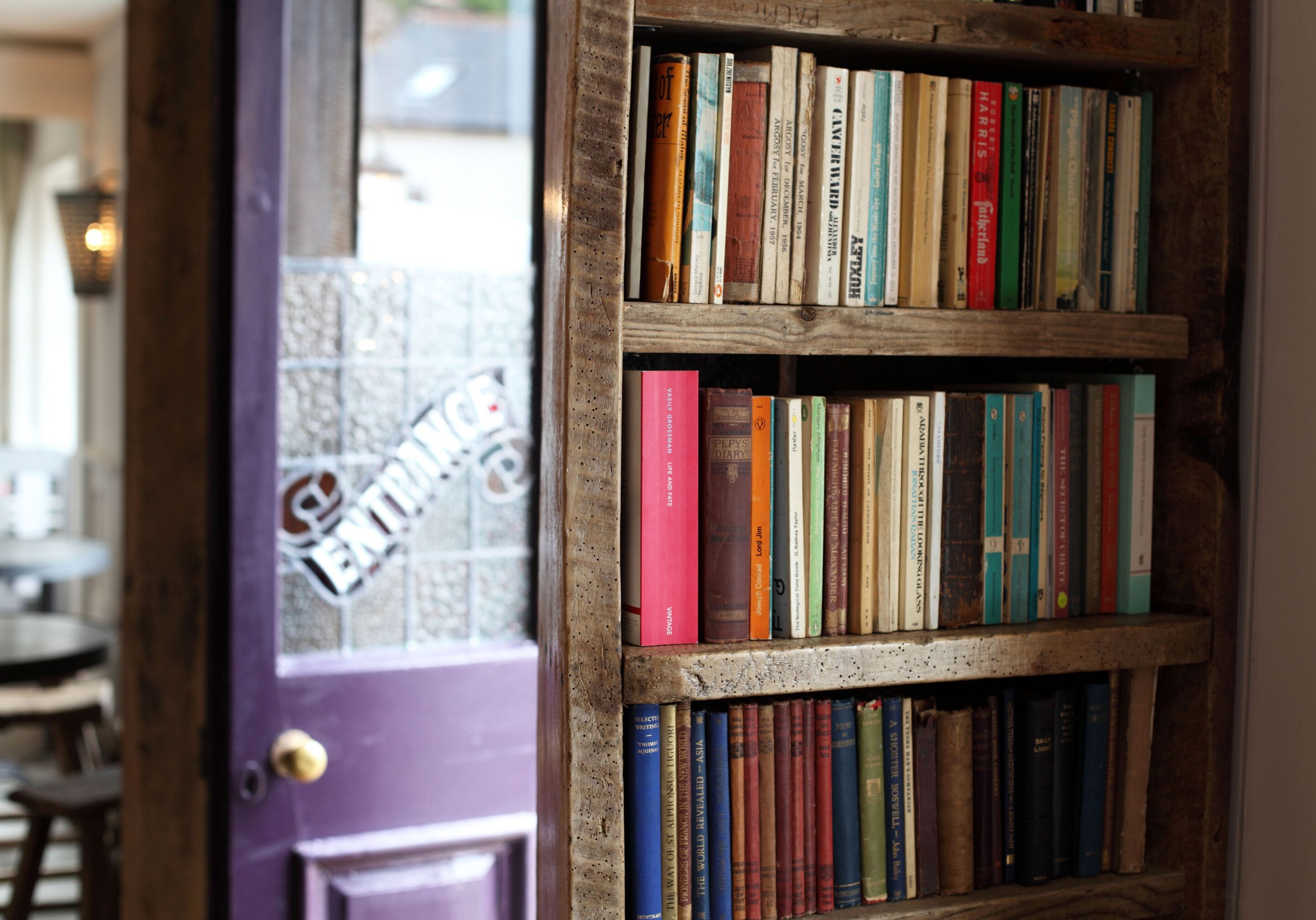 A bookshelf filled with books in a room with a purple door and tiled walls.