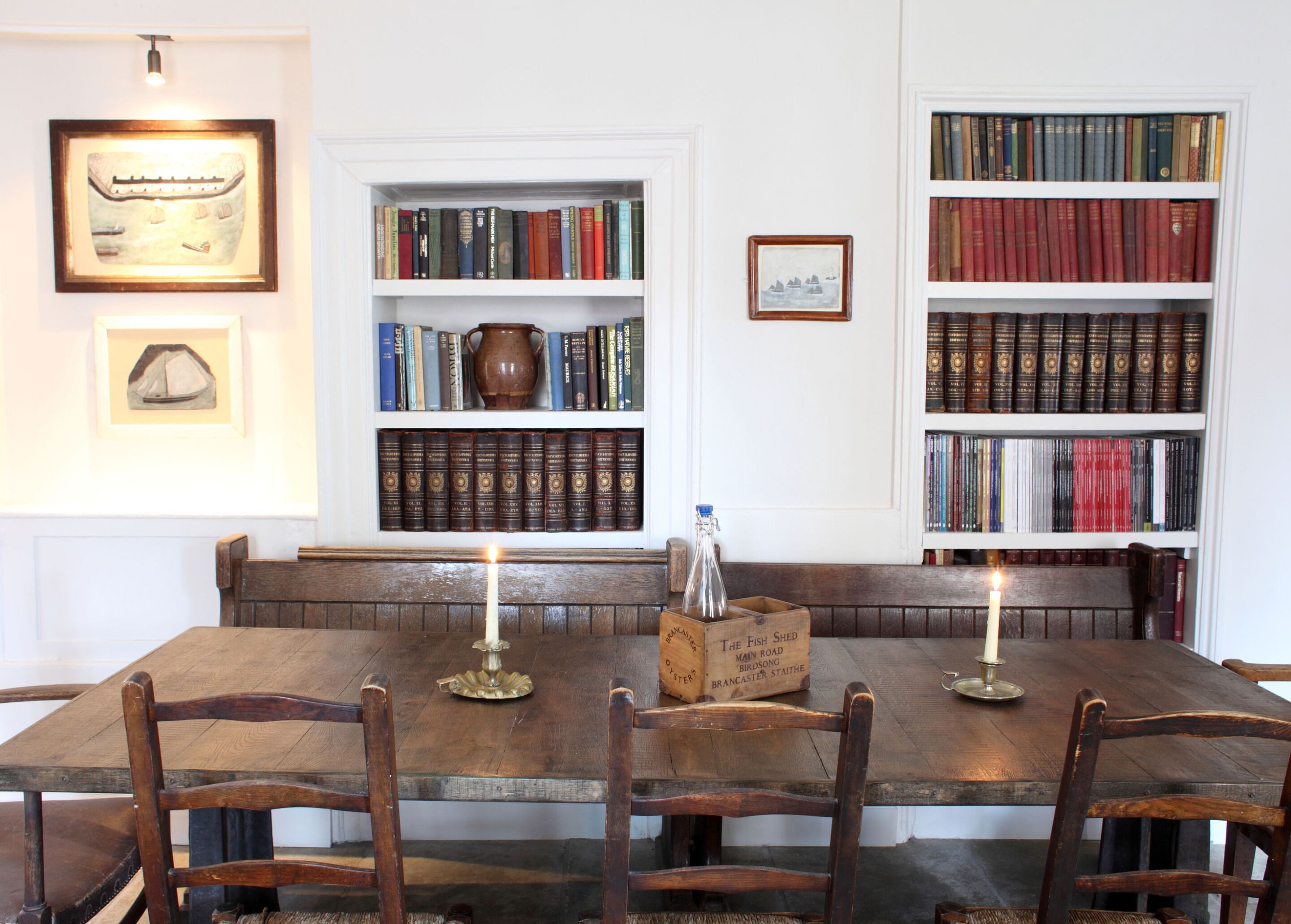 A wooden dining table with four chairs, surrounded by bookshelves filled with books.