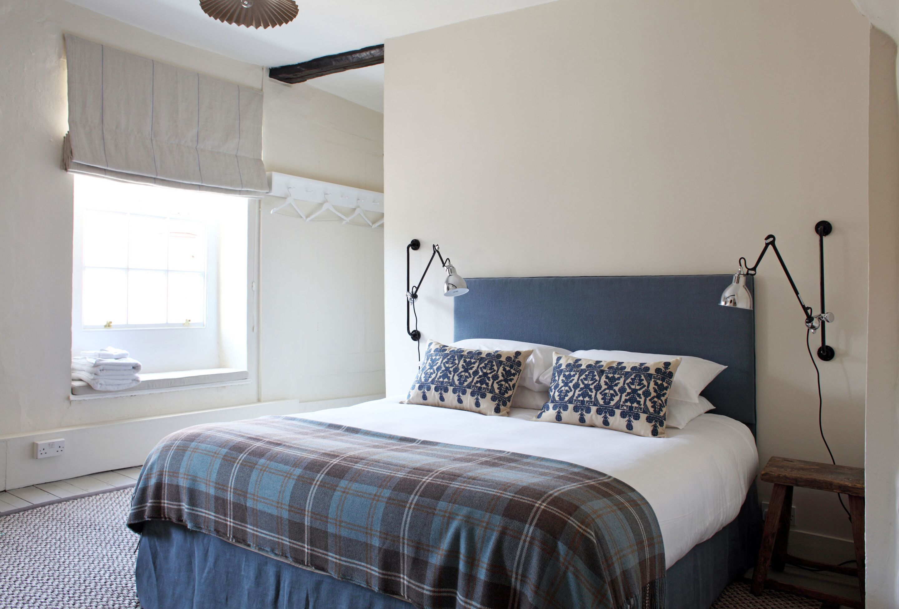 A bedroom with a bed, two bedside lamps, a window with a curtain, and a small wooden stool.
