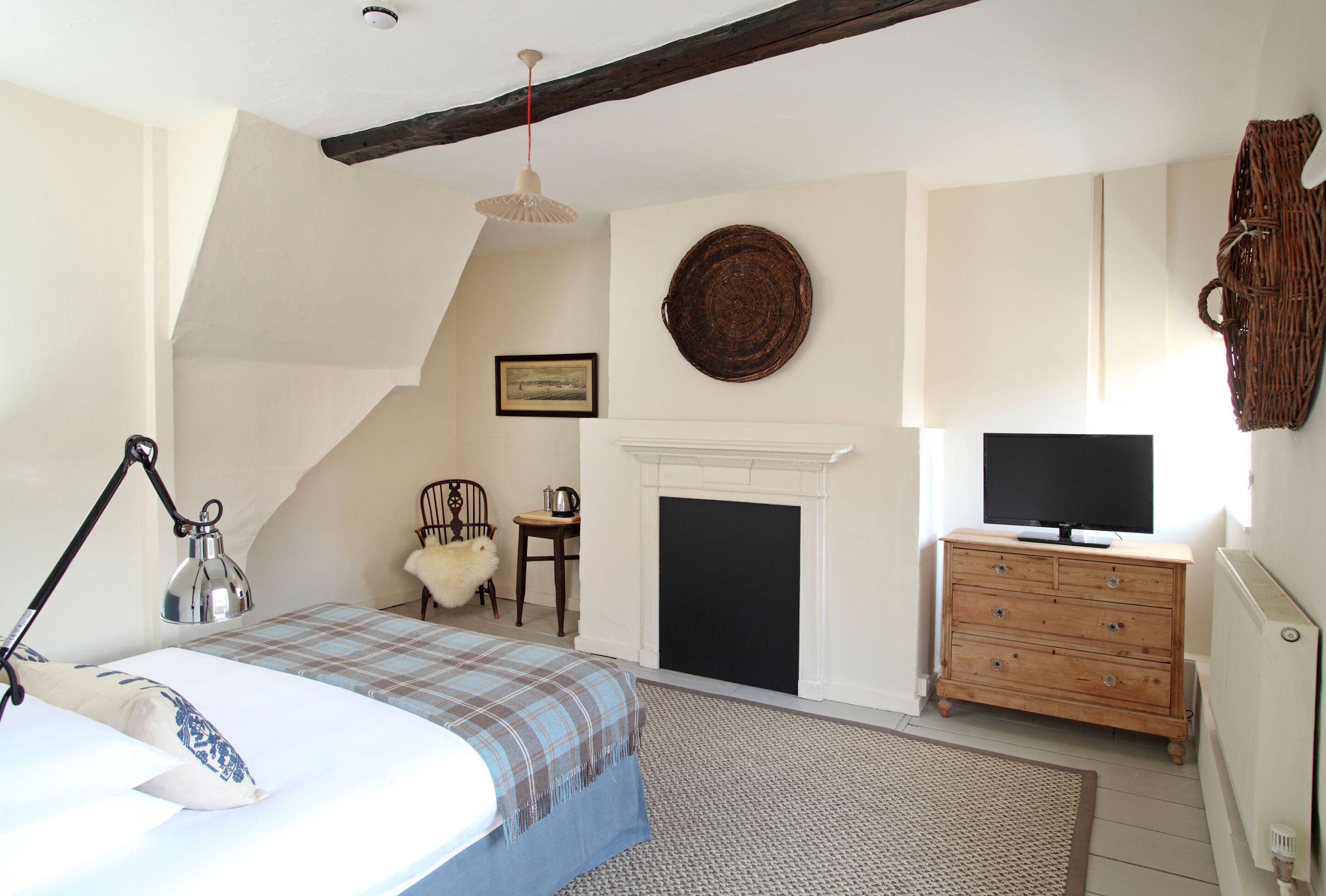 Un dormitorio con cama, cómoda, televisor, chimenea y una silla.
