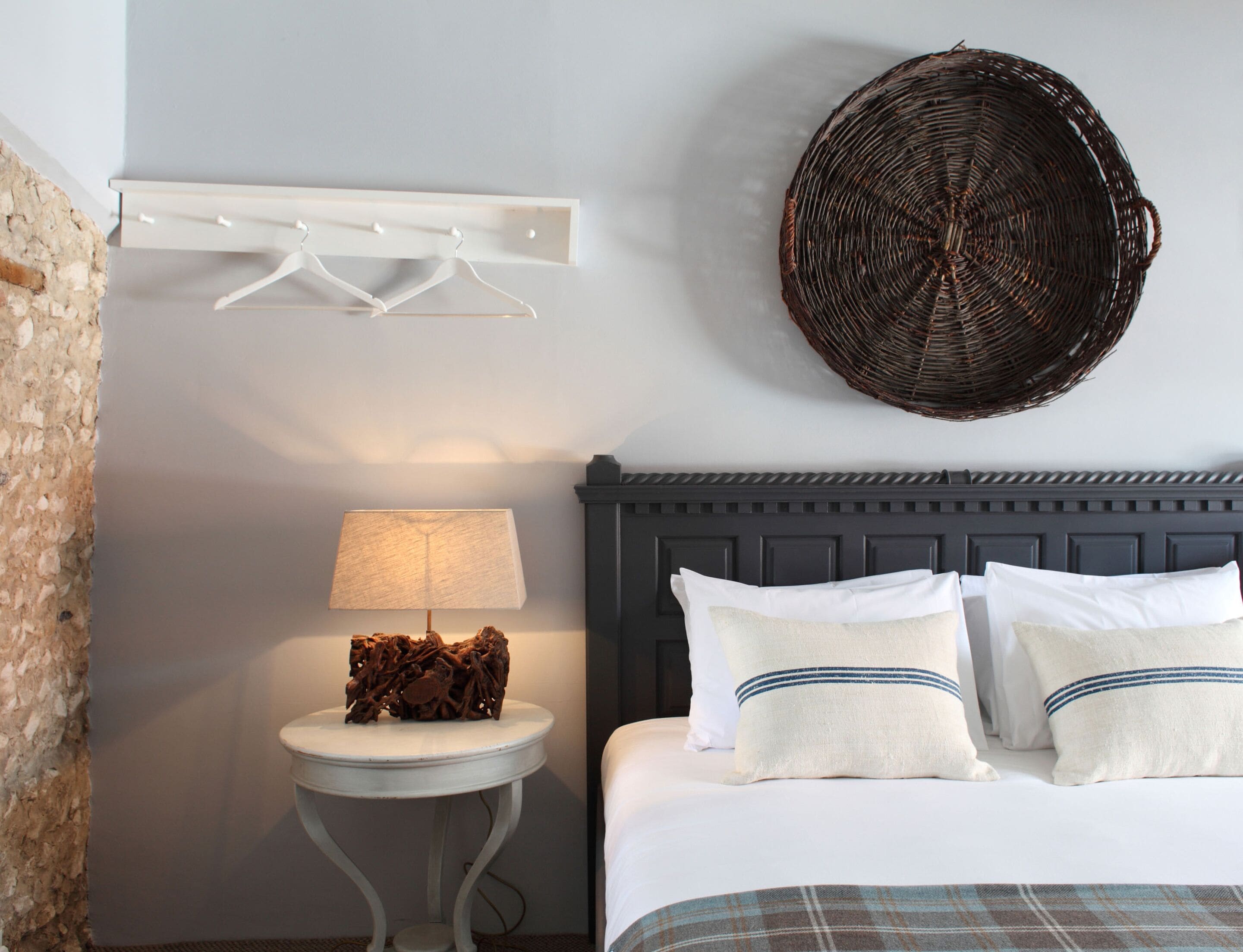 A bedroom with a bed, a bedside table with a lamp, a wall-mounted wicker basket, and a white coat rack.
