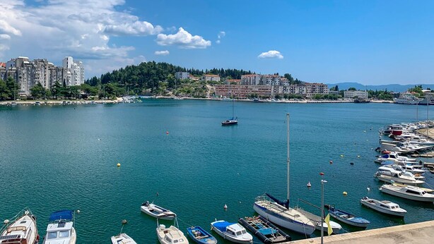Un puerto deportivo con barcos amarrados, cielo despejado y un paisaje urbano al fondo.