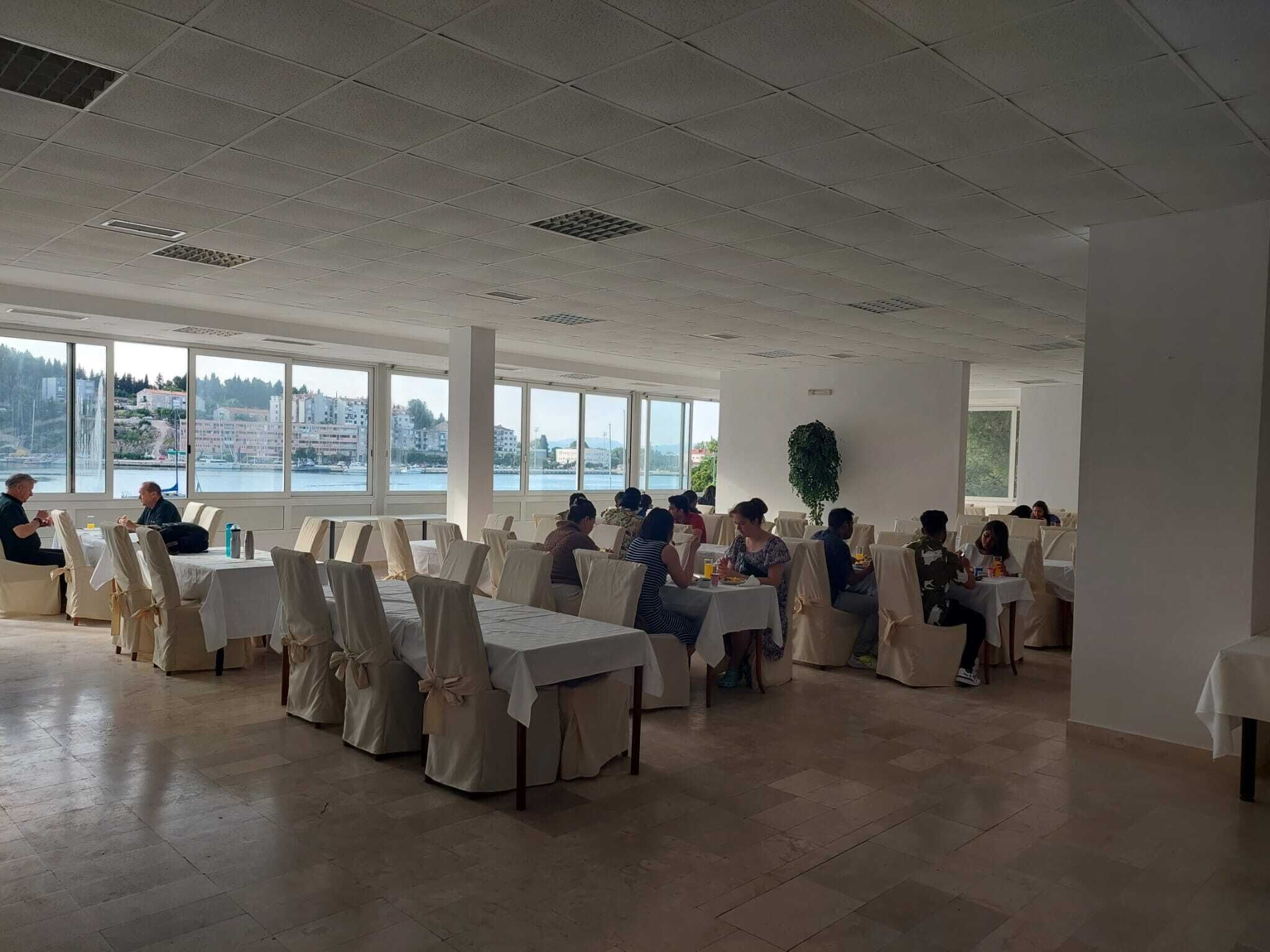 Una sala conferenze con tavoli e sedie, ampie finestre vista edifici e acqua, e un soffitto con illuminazione a incasso.