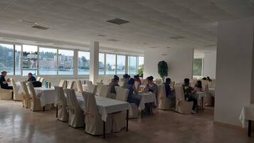 Una sala conferenze con tavoli e sedie, ampie finestre vista edifici e acqua, e un soffitto con illuminazione a incasso.