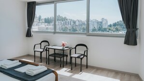 Una habitación de hotel con una cama, una pequeña mesa con sillas y un ventanal con cortinas.