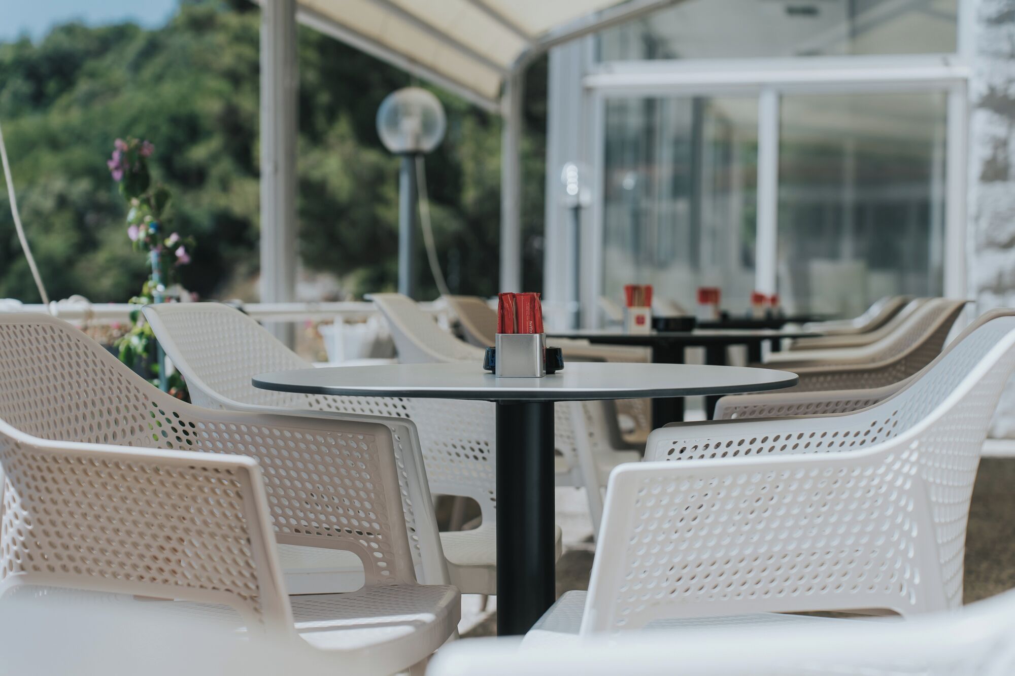 Un área de estar al aire libre cubierta con sillas y mesas de plástico blanco, algunas con vasos rojos.