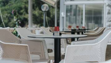 Un área de estar al aire libre cubierta con sillas y mesas de plástico blanco, algunas con vasos rojos.
