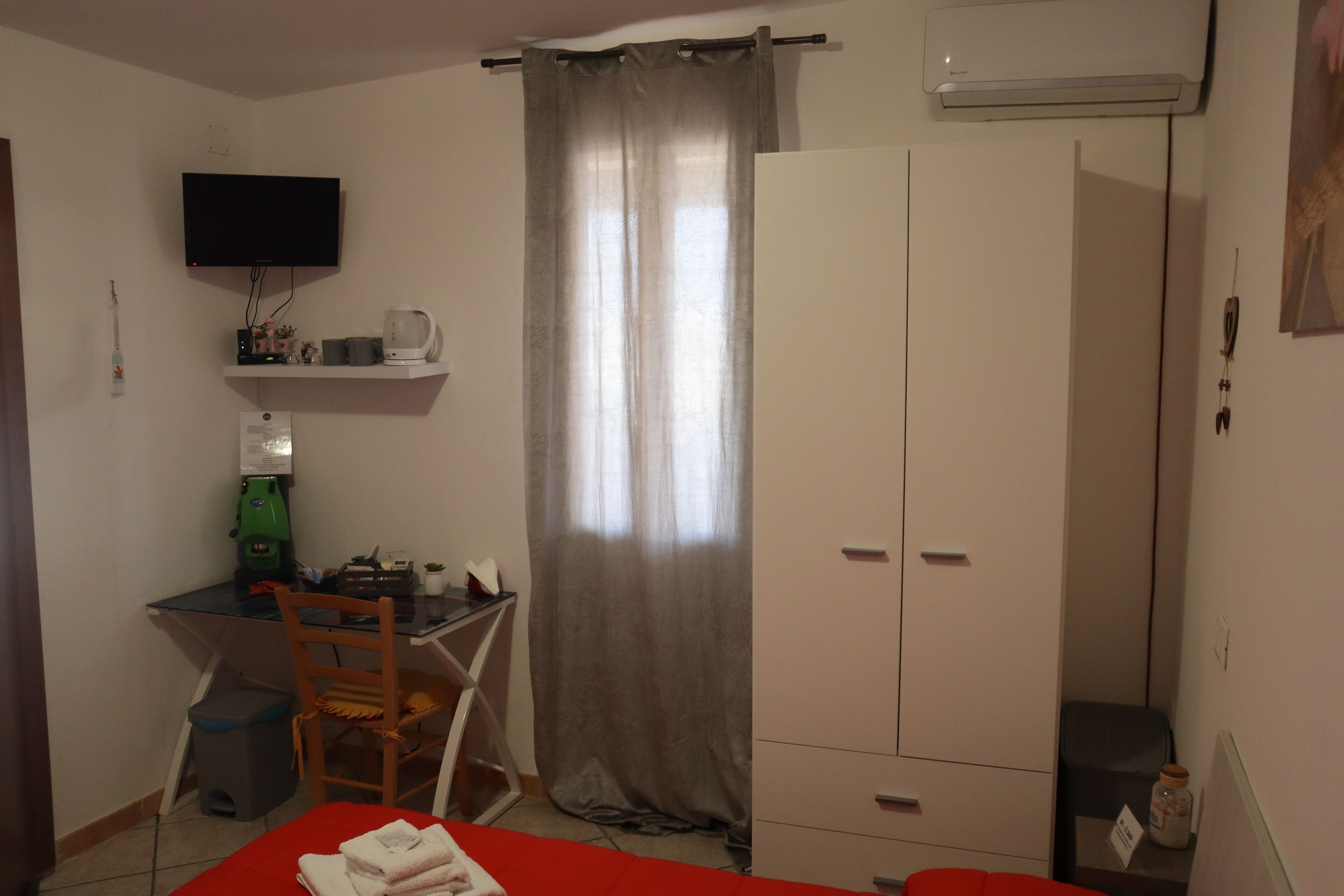 Une pièce comprenant un lit, un bureau, une chaise, une armoire, un téléviseur et une fenêtre avec des rideaux.
