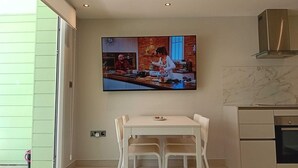 A modern kitchen with a dining area, a large TV mounted on the wall, and a view of the outside. - Marina Club Adriatic, Gibraltar - Studio Apartment (Gibraltar)