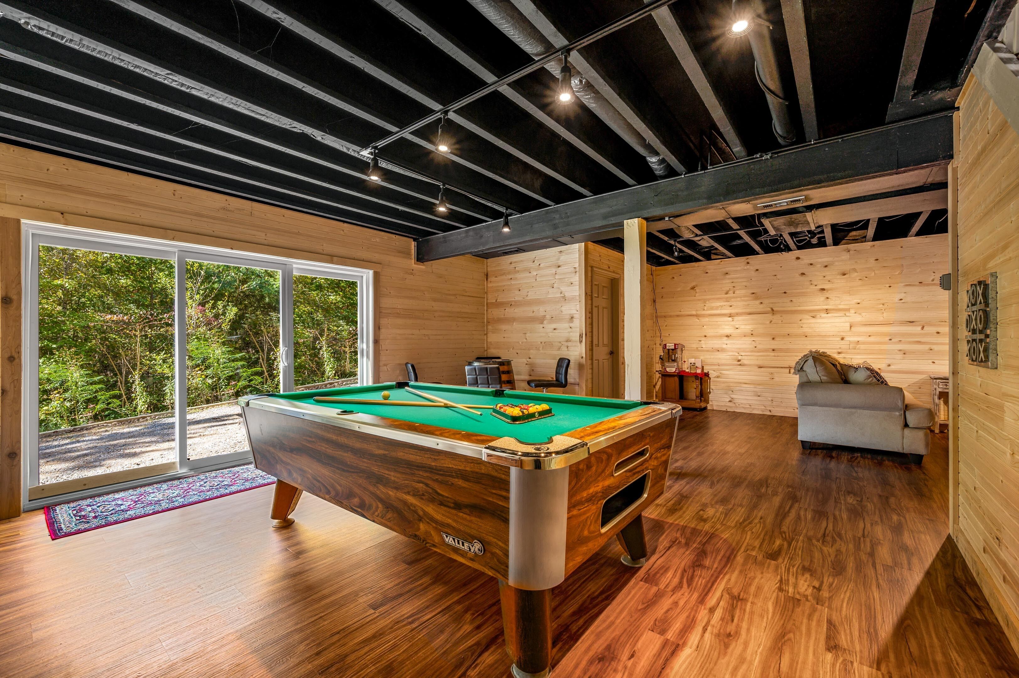 Une table de billard dans une pièce aux murs en bois et dotée d’une grande fenêtre.