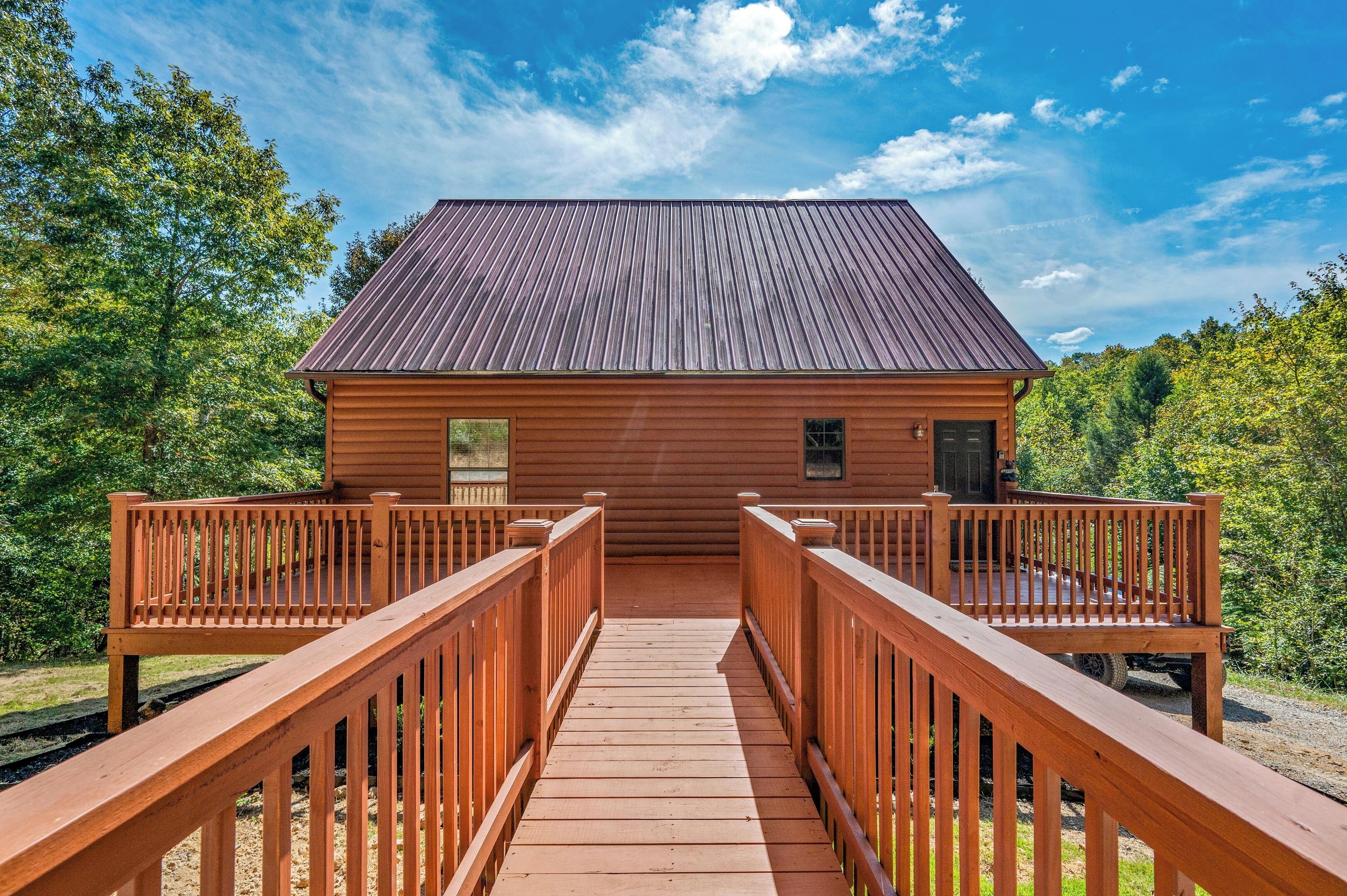 Une cabane en bois avec un toit en métal, un porche à l’avant et une terrasse en bois menant à l’entrée.