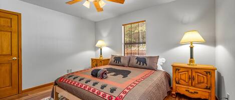 A bedroom with a bed, wooden nightstands, a ceiling fan, a window, and a door.