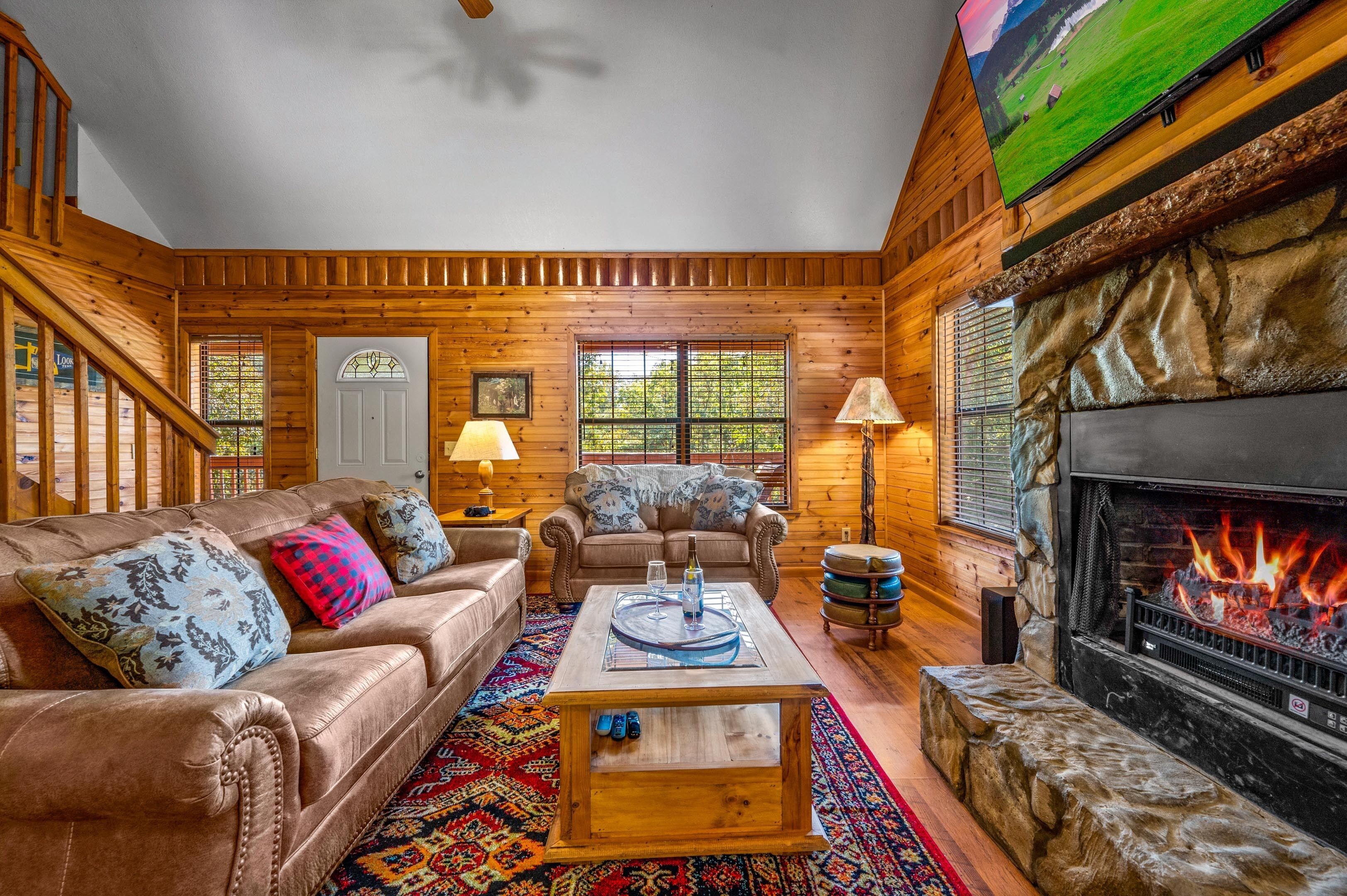 A cozy log cabin interior with a leather sofa, a fireplace, and a television mounted on the wall.