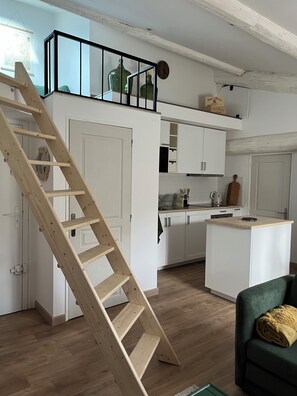 Een kleine keuken met witte kasten, een houten trap en een groene bank.