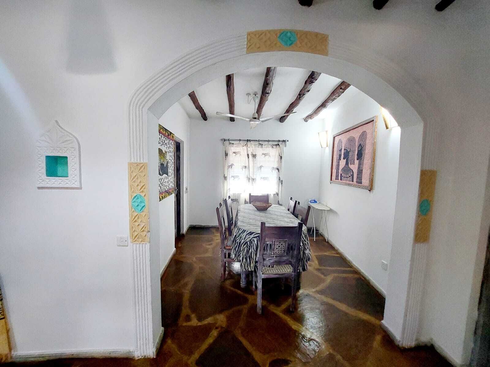 A dining area with a table set for four, a ceiling fan, and a patterned floor.
