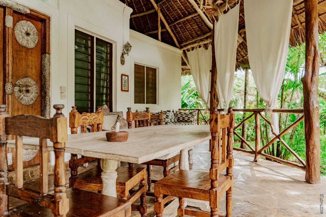 Una mesa de comedor de madera con bancos, una puerta de madera con placas decorativas y una estructura de techo de paja.