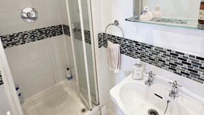 Ein Badezimmer mit Duschkabine aus Glas, einem weißen Waschbecken mit zwei Wasserhähnen und einem Spiegel darüber.