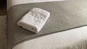 Ein ordentlich bezogenes Bett mit einer grauen Decke und einem gefalteten weißen Handtuch.