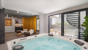 Habitación de hotel moderna con zona de spa, que incluye una bañera de hidromasaje, un espacio de descanso y vistas al balcón exterior.