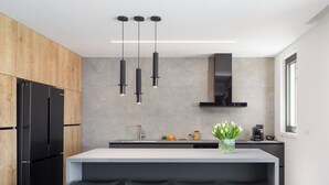 Una cocina moderna con una isla central, taburetes negros, horno empotrado e iluminación colgante.