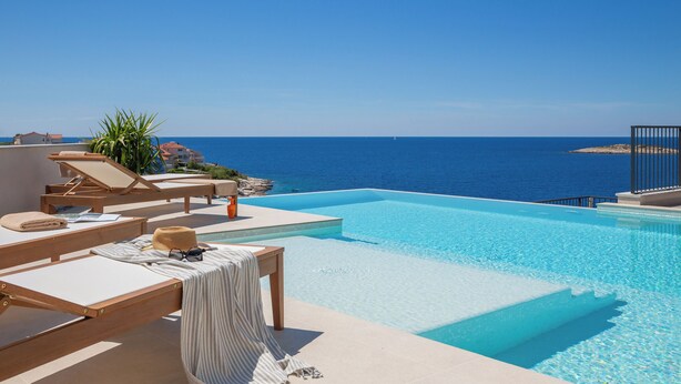 Zona de piscina con sillones de descanso y vista al mar.