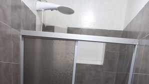 A bathroom with a toilet, a shower stall, and tiled walls. - Suíte Barros (Navegantes)